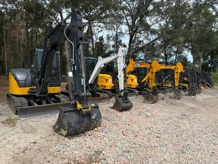 A line of various mini excavators with buckets, including black, white, and yellow models.