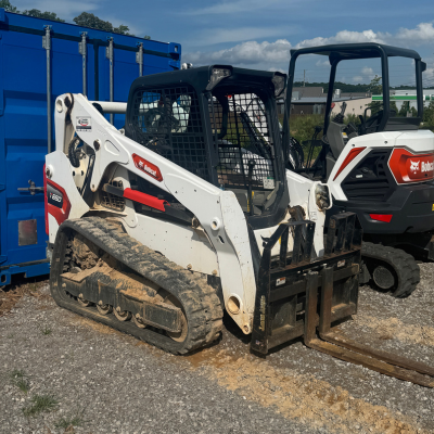 Bobcat T650 skid steer with rubber tracks parked on a jobsite with dirt and pallets in view.