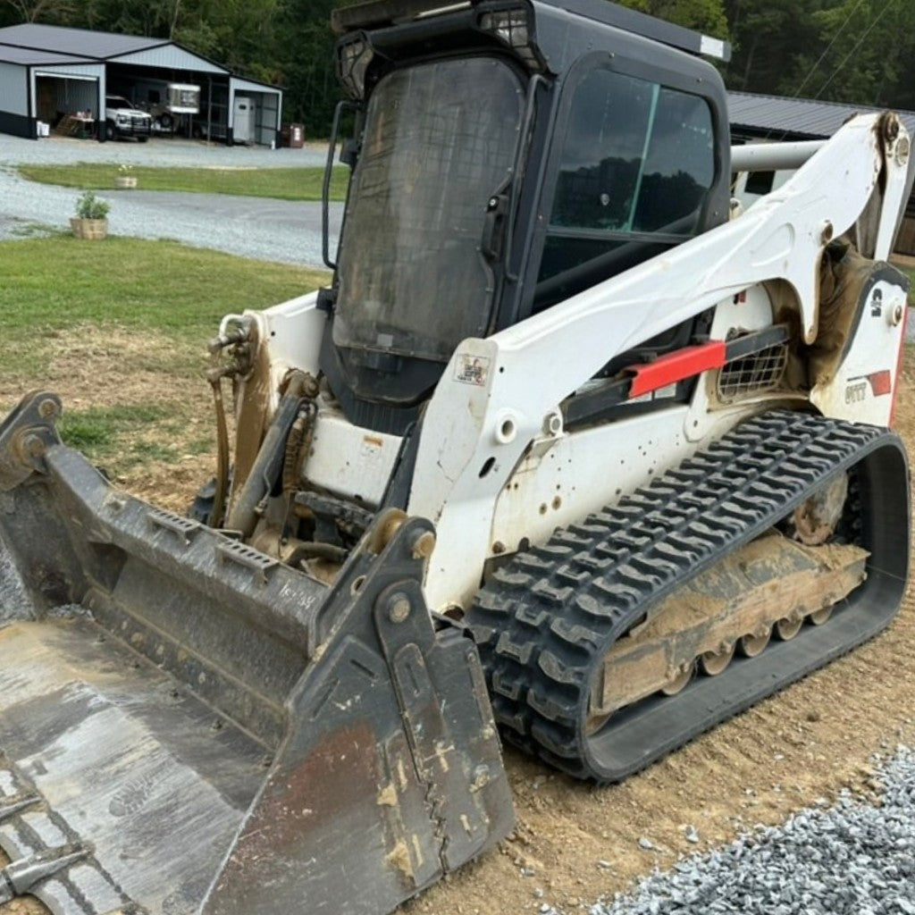 Heavy-duty replacement rubber tracks on a Bobcat T870 track loader working land-clearing terrain.