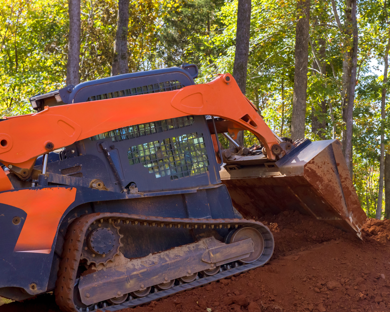 Kubota SVL75-2 compact track loader pushing dirt on a slope — heavy-duty rubber tracks digging into clay soil