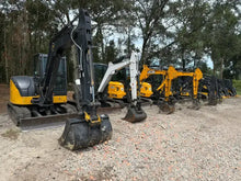 Row of yellow and black construction excavators on gravel at outdoor equipment lot