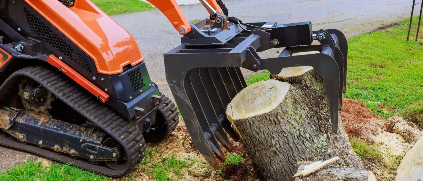 Compact track loader equipped with heavy-duty rubber tracks gripping and moving a tree log during landscaping work.