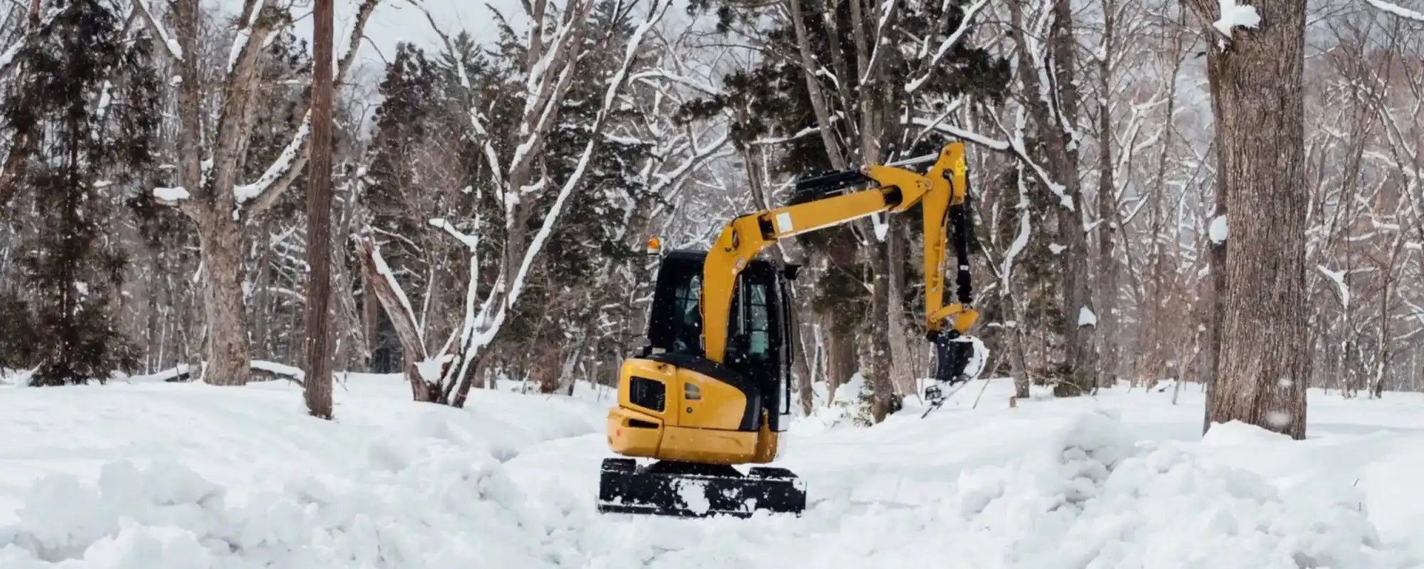 Yellow compact excavator clearing snow.